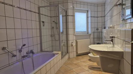 Ein modernes Badezimmer mit einer Badewanne, Dusche und Toilette. Die Wände sind mit hellen Fliesen gefliest und es gibt ein Fenster für Tageslicht.