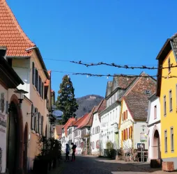 Eine malerische Straße mit bunt gestrichenen Häusern und einem klaren blauen Himmel. Im Hintergrund sind sanfte Hügel zu sehen.