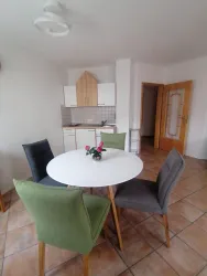 Ein helles Esszimmer mit einem runden Tisch und vier Stühlen in verschiedenen Farben. Im Hintergrund sieht man eine kleine Küchenzeile mit praktischer Einrichtung.