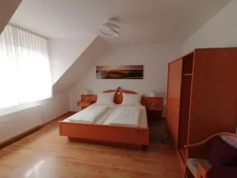 Ein gemütliches Schlafzimmer mit einem Doppelbett und Holzschränken. Große Fenster lassen viel Tageslicht herein.