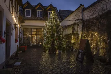 Ein malerischer Innenhof mit einem festlich geschmückten Weihnachtsbaum und warmem Licht. Die Umgebung ist mit Lichtern dekoriert und vermittelt eine gemütliche Atmosphäre.