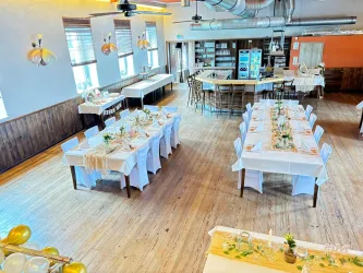 Ein helles Restaurant mit Holzboden und elegant gedeckten Tischen. Im Hintergrund befindet sich eine Bar mit Stühlen und weiteren Sitzbereichen.