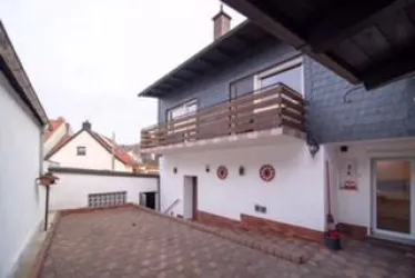 Ein modernes Haus mit einem Balkon und einem gepflasterten Hof. Die Umgebung ist ruhig und gepflegt.
