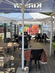 Ein überdachter Außenbereich mit mehreren Tischen und Stühlen. Der Platz ist ordentlich, mit einem Blick auf eine bunte Wand im Hintergrund.