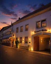 Ein charmantes Gebäude mit warmem Licht, das in der Abenddämmerung strahlt. Die Straße ist ruhig und von sanften Wolken am Himmel umgeben.