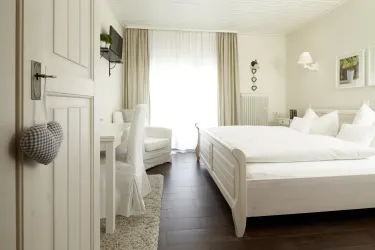 Ein helles und modernes Schlafzimmer mit einem weißen Bett und großen Fenstern. Es gibt einen kleinen Schreibtisch und einen gemütlichen Stuhl im Raum.