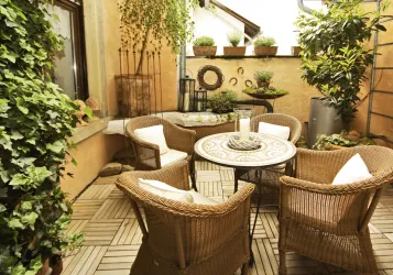 Eine gemütliche Terrasse mit einem runden Tisch und vier Korbstühlen. Umgeben von Pflanzen und einer entspannten Atmosphäre.