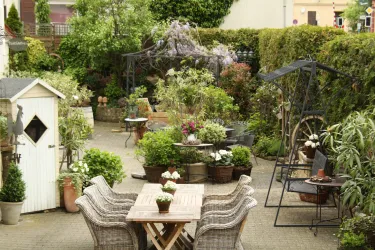 Ein schöner Garten mit vielen Pflanzen und Blumen. Es gibt einen Tisch mit Stühlen und einen kleinen Gartenhaus.