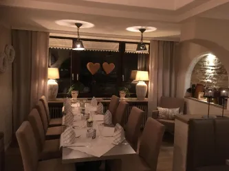 Ein eleganter Essraum mit einem langen Tisch und bequemen Stühlen. Die sanfte Beleuchtung und die herzförmigen Fenster dekorieren die Atmosphäre.