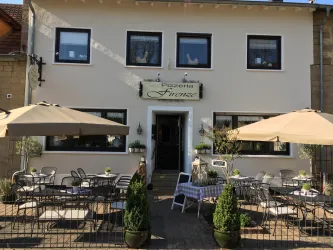Ein gemütliches Restaurant mit dem Namen "Pizzeria Finesse". Es gibt einen Außenbereich mit Tischen, Sonnenschirmen und Pflanzen.
