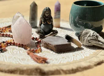 Ein dekorativer Tisch mit spirituellen Gegenständen, darunter Kristalle, eine Statue und ein Becher. Die Anordnung ist auf einem hellen Tuch gelegt und vermittelt ein Gefühl von Ruhe und Harmonie.