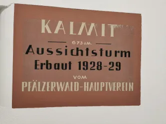 Ein Schild mit der Aufschrift „Kalmit, 673 m, Aussichtsturm, erbaut 1928-29, vom Pfälzerwald-Hauptverein“. Es zeigt Informationen über den Aussichtsturm Kalmit.