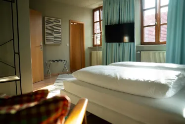 Ein helles Schlafzimmer mit zwei Einzelbetten und großen Fenstern. Die Einrichtung ist modern und freundlich, mit einem Fernseher an der Wand.