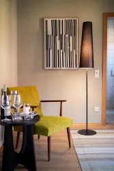 Ein modernes Wohnzimmer mit einem gelben Stuhl und einer eleganten Stehlampe. Auf dem Tisch stehen Gläser und eine Flasche.