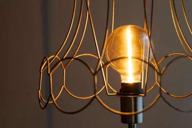 Eine moderne Lampe mit einem warmen Licht und einem minimalistischen Drahtdesign. Der Glühbirne ist gut sichtbar und strahlt ein einladendes Licht aus.