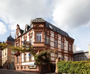 Ein historisches Gebäude mit roter Fassade und eleganten Fenstern. Umgeben von grüner Vegetation und einem bewölkten Himmel.