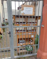 Ein Holzregal mit verschiedenen Gläsern steht hinter einem Gittertor. Es gibt ein Schild mit der Aufschrift "Selbstbedienung".