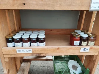 Ein Holzregal mit Einmachgläsern. Links stehen mehrere Gläser mit Marmelade und rechts einige mit Honig.