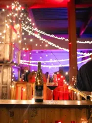 Eine stilvolle Bar mit Lichtern und einer festlichen Atmosphäre. Auf dem Tisch stehen eine Flasche Wein und ein Weinglas.