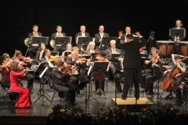Ein Orchester spielt auf einer Bühne. Der Dirigent leitet die Musiker, während sie ihre Instrumente spielen.