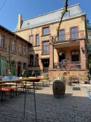Ein einladender Innenhof mit alten Ziegelgebäuden und Tischen im Freien. Die Sonne scheint und schafft eine gemütliche Atmosphäre.