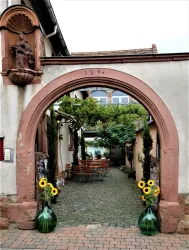 Ein bezaubernder Innenhof mit einem großen Torbogen. Auf der Pflastersteingasse stehen zwei große Vasen mit Sonnenblumen.