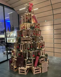 Ein festlich geschmückter Weihnachtsbaum aus Holzkisten, geschmückt mit roten Kugeln und Lichtern. Der Baum steht in einem modernen Raum mit großen Fenstern.