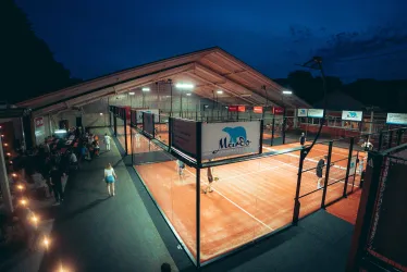 Ein modernes Tennis- und Padel-Center bei Nacht mit beleuchteten Plätzen. Menschen stehen an den Seiten und genießen die Atmosphäre.