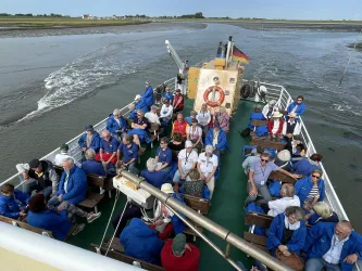 Eine Gruppe von Menschen sitzt auf einem Boot, das durch ein ruhiges Gewässer fährt. Die Passagiere tragen überwiegend blaue Jacken und genießen die Aussicht.