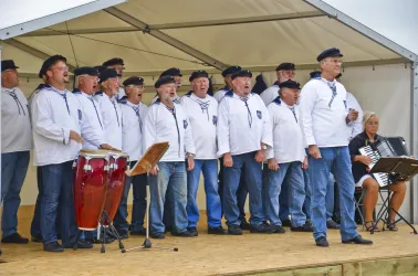 Eine Scharfmannschaft singt auf einer Bühne. Im Hintergrund spielt eine Frau Akkordeon.