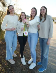 Vier Frauen stehen draußen und halten ein Flasche Sekt in der Hand. Sie lächeln und genießen das schöne Wetter.