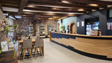 Ein Glas Sekt wird in einem Weinberg eingeschenkt. Im Hintergrund sind Trauben und Weinreben zu sehen.