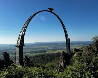 Ein schmiedeeisernes Tor mit einem Aussichtspunkt auf die Landschaft. Der Himmel ist klar und die Umgebung ist grün und hügelig.