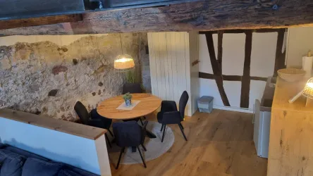 Ein gemütlicher Essbereich mit einem runden Tisch und schwarzen Stühlen. Die Wände haben einen rustikalen Look mit sichtbarem Holz.