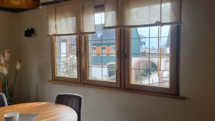 Ein gemütlicher Raum mit Holzfenstern und einem Blick auf eine stilvolle Außenansicht. Auf einem Tisch stehen dekorative Elemente und Pflanzen.