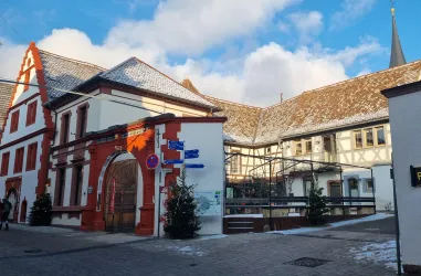 Ein historisches Gebäude mit roten und weißen Elementen. Die Szene zeigt eine malerische Straße unter einem klaren Himmel.