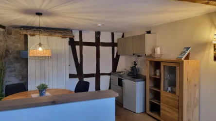 Ein gemütlicher Raum mit moderner Küche und rustikalen Holzwänden. Der runde Tisch und die sanfte Beleuchtung schaffen eine einladende Atmosphäre.