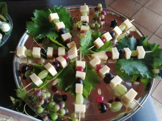Ein dekorativer Teller mit Käsewürfeln und frischen Trauben. Die Snacks sind auf Weinblättern angerichtet und bilden eine ansprechende Präsentation.
