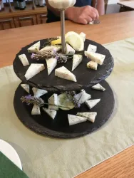 Ein zweistufiger Käseteller aus schwarzem Stein, dekoriert mit Kräutern und Zitronenscheiben. Die Käsestücke sind kunstvoll angeordnet und ansprechend präsentiert.