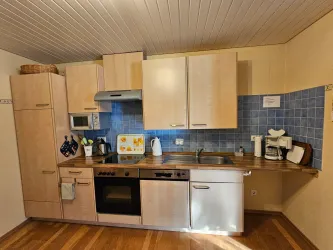 Eine moderne Küche mit hellen Holzschränken und blauen Kacheln. Sie ist ausgestattet mit Geräten wie Herd, Ofen und Wasserkocher.