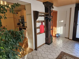 Ein heller Flur mit Fliesenboden und einem Holzständer. Auf dem Ständer hängen eine rote Tasche und verschiedene Gegenstände.