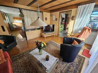 Ein gemütliches Wohnzimmer mit einem roten und einem schwarzen Sessel. Ein Couchtisch mit Blumen und einem Fernseher in der Ecke.
