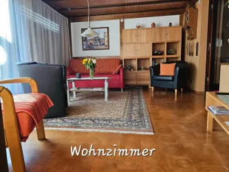 Ein gemütliches Wohnzimmer mit roten und schwarzen Möbeln. Der Raum hat einen orientalischen Teppich und viel Tageslicht.