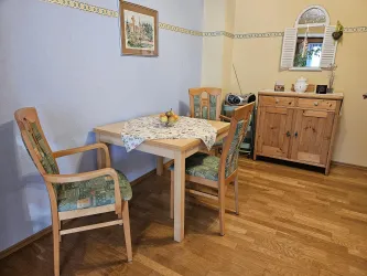 Ein gemütlicher Essbereich mit einem hellen Tisch und zwei Stühlen. Im Hintergrund steht eine Holzkommode und eine Wandspiegel.