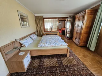 Ein gemütliches Schlafzimmer mit einem großen Bett und einem geschmackvollen Teppich. Holzschränke und ein Fenster lassen den Raum hell und einladend wirken.