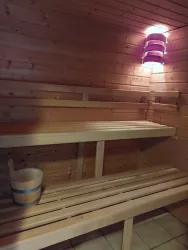 Eine gemütliche Sauna mit Holzbänken und sanfter Beleuchtung. Neben den Bänken steht ein Eimer für Wasser.
