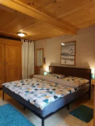 Ein gemütliches Schlafzimmer mit einem großen Doppelbett und bunten Bettdecken. Holzvertäfelung und ein Kleiderschrank schaffen eine warme Atmosphäre.