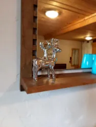Eine silberne Rentierfigur steht auf einem Holzregal vor einem Spiegel. Im Hintergrund sind bläuliche Gläser und ein schöner Innenraum sichtbar.