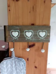 Ein dekoratives Holzpanel mit drei herzförmigen Anhängern und Haken. Es ist an einer Wand montiert und verleiht dem Raum einen gemütlichen Touch.