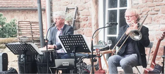 Zwei Musiker spielen live auf einer Bühne im Freien. Der Sänger ist am Mikrofon, während der Trompeter sein Instrument spielt.